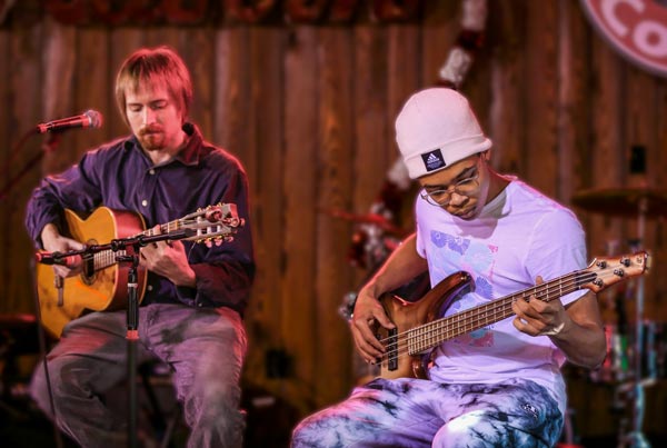 A teacher and bass guitar student perform together on stage as a music recital