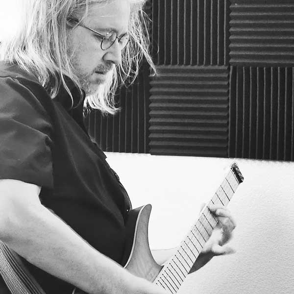 Man with shoulder-length hair plays electric guitar