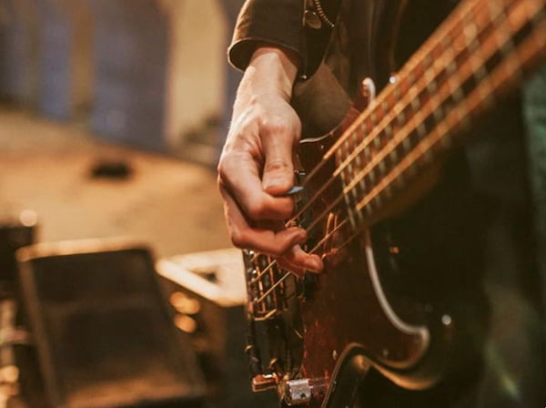 closeup of a hand holding a pick, ready to strum on the strings of a brown bass guitar