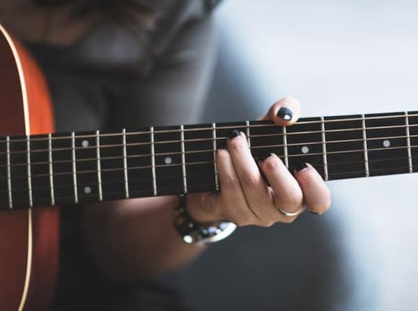 closeup of a person's hand resting on the frets of an acoustic guitar.