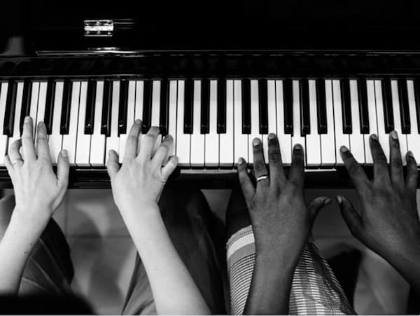 balck and white photo closeup of two piano players' hands (one shite, one black) sitting next to each other playing the same piano.
