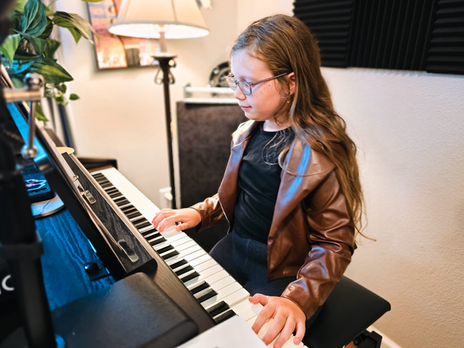Young girl with long hair wearing a leather jacket smiles while playing a piano
