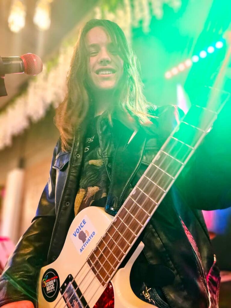Teen boy with long hair plays bass guitar on stage at a recital in Cedar Park
